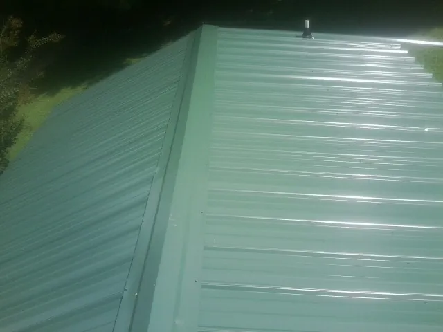 New green metal panels meeting at the ridge of a roof — Flat Roof Repair work by our crew in Garden City